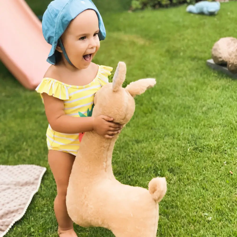 Child cuddling a rusty brown soft toy-pillow alpaca that’s 50cm tall