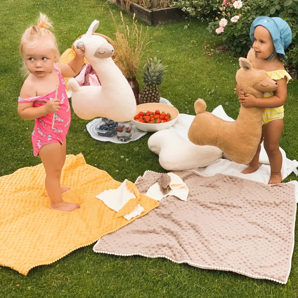 Two toddlers joyfully hugging rusty brown soft toy-pillow alpacas, perfect for cuddles