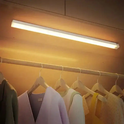 Magnetic LED Light Bar in warm white light illuminating closet rod with hanging clothes